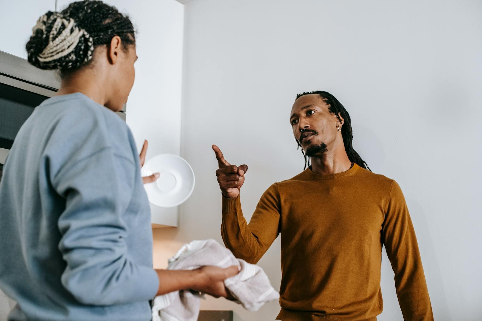 Annoyed African American male with finger up menacing to anonymous female partner while arguing in kitchen and looking at each other